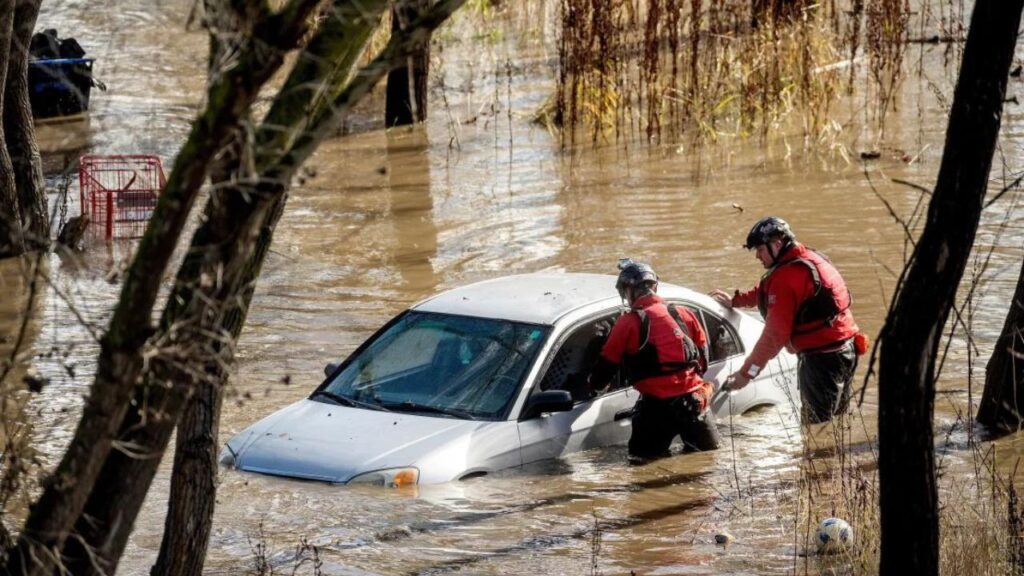 Search and rescue personnel in San Jose, California, look into an automobile that is engulfed in floodwaters.