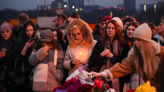 People lay flowers and light candles standing next to the Crocus City Hall, on the western edge of Moscow, Russia, Saturday, March 23, 2024.