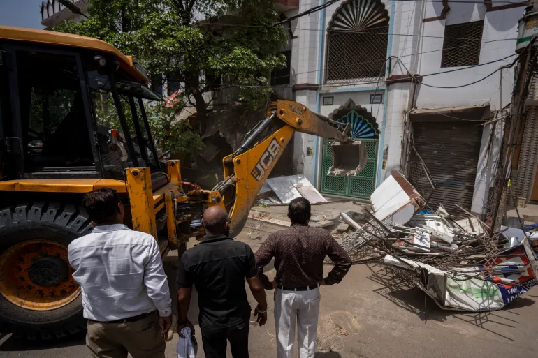 Officials watch as a bulldozer razes the wall of a local mosque in New Delhi’s northwest Jahangirpuri neighbourhood, on Wednesday, April 20, 2022. Rights groups have accused Indian authorities of a growing pattern of ‘bulldozer justice’ aimed at punishing Muslims.